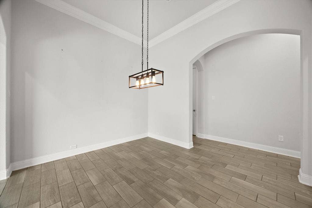 Spacious room featuring wood-finish flooring, white wall paint, and white crown molding