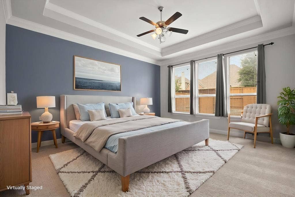 Spacious room featuring tray ceiling, ceiling fan with light fixture, three large windows with blinds, and neutral carpet flooring