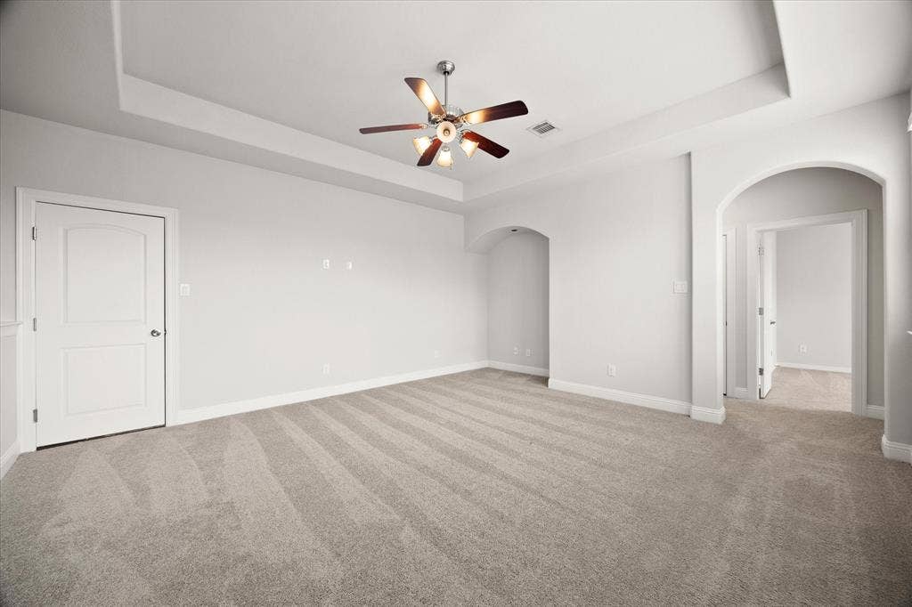 Spacious room featuring a tray ceiling, recessed alcoves, and light neutral carpeting