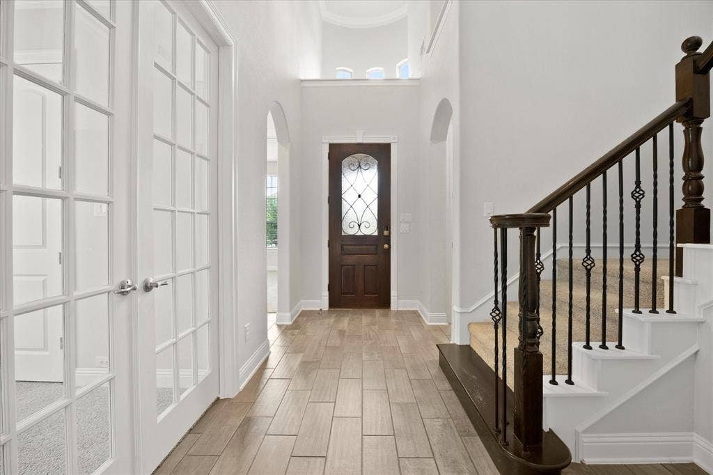 Foyer with wood-finish tile flooring, a dark wood entry door with decorative glass, and a traditional staircase featuring dark wood newel posts and wrought iron balusters