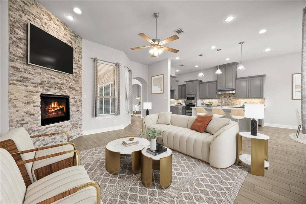 Open-concept living area featuring a stone accent wall, fireplace, recessed lighting, wood-finish flooring, and a kitchen with gray cabinetry