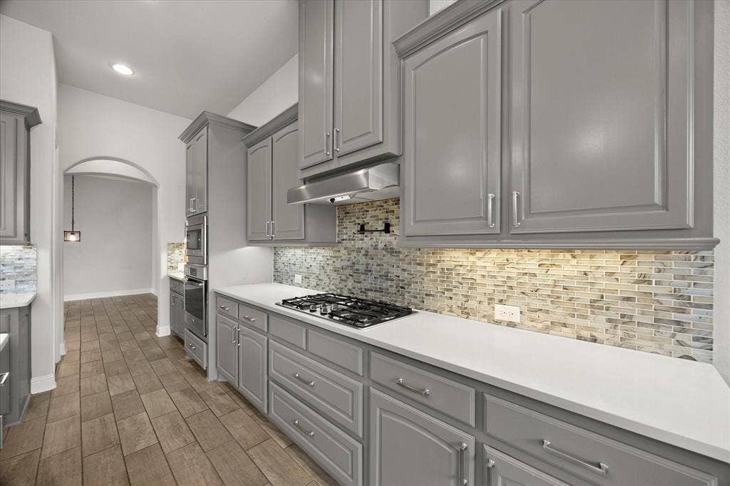 Kitchen featuring gray cabinetry, light countertops, a mosaic tile backsplash, stainless steel appliances, and wood-finish flooring