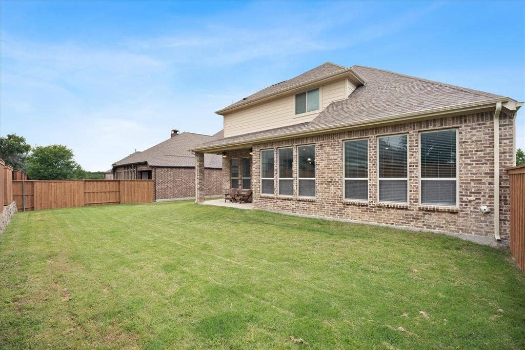 Expansive backyard featuring a manicured lawn, full privacy fencing, and a covered patio