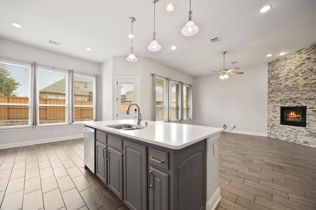 Kitchen island featuring a stainless steel sink with a high-arc faucet, white countertop, and gray cabinetry