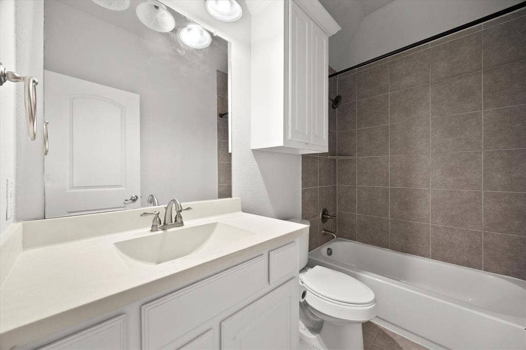 Bathroom featuring a white vanity with an integrated sink, brushed nickel faucet, large wall mirror, and overhead vanity lighting