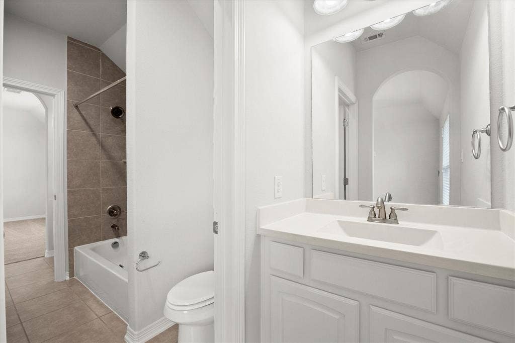 Full bathroom featuring a white vanity with integrated sink, brushed nickel fixtures, a tub/shower combination with tiled surround, and ceramic tile flooring