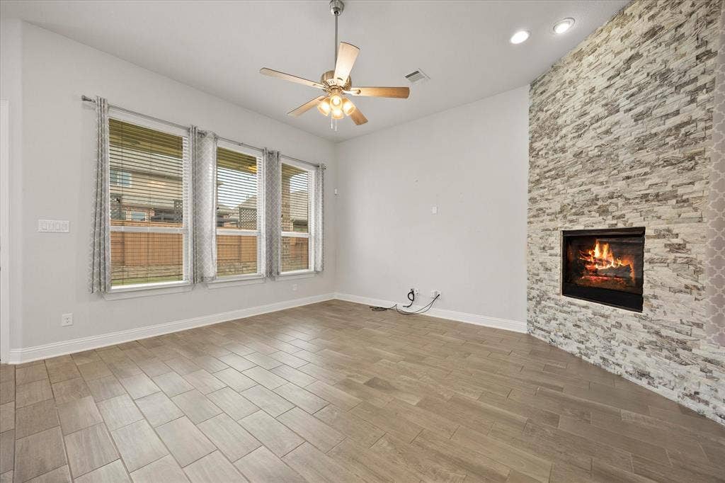 Living area featuring a floor-to-ceiling stacked stone fireplace, wood-finish tile flooring, a ceiling fan, and three large windows