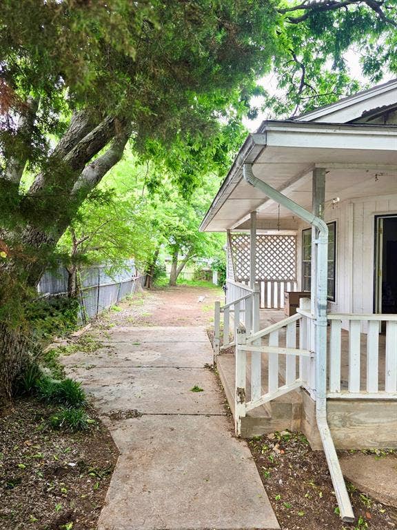 417 W Huffman Street, Krum, TX 76249 Covered porch with white railings and lattice detailing, featuring a concrete walkway and mature trees