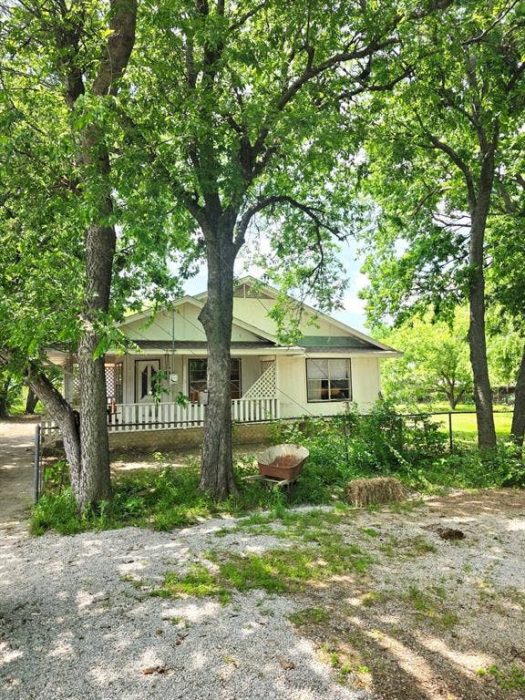 417 W Huffman Street, Krum, TX 76249 Charming single-story property featuring a front porch with white railings, a light-colored exterior, and a prominent green roof