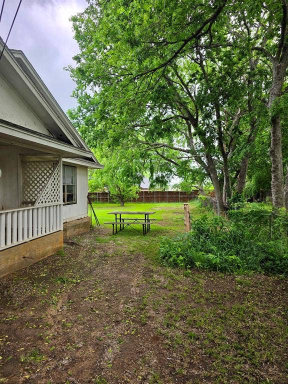 417 W Huffman Street, Krum, TX 76249 Spacious backyard featuring mature trees, a wood privacy fence, and an exterior wall with lattice detailing