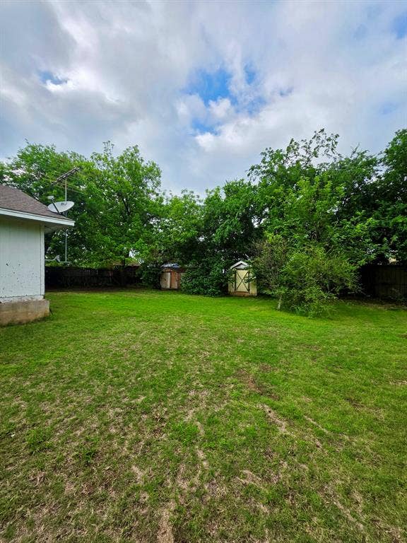 417 W Huffman Street, Krum, TX 76249 Spacious backyard featuring a grass lawn, mature trees, and two storage sheds