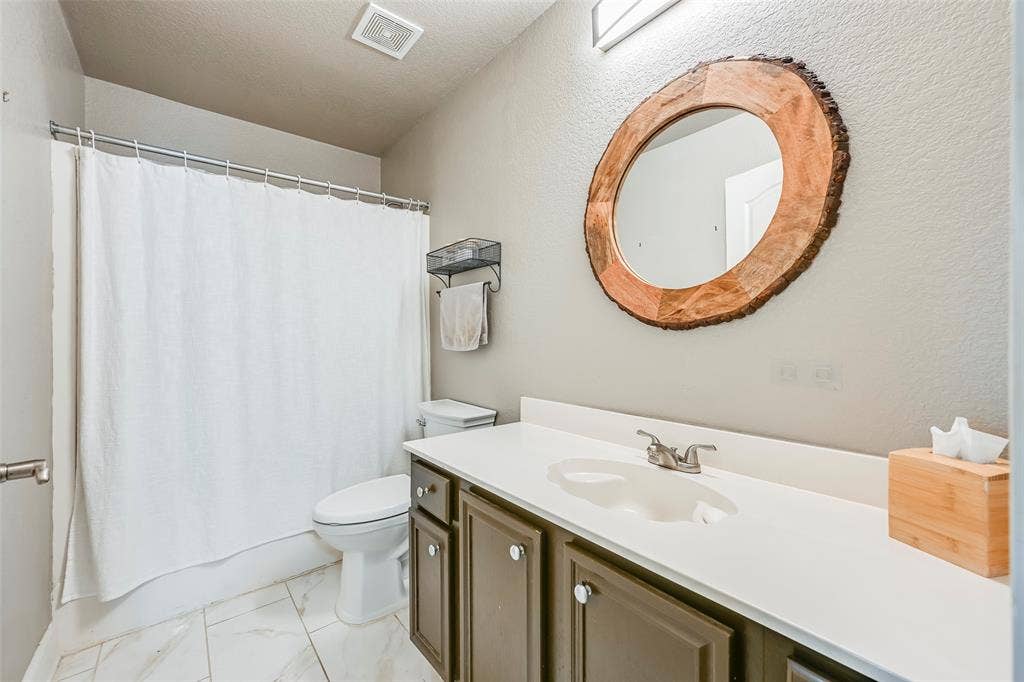 Bathroom featuring a single vanity with a white countertop, a circular mirror with a wood frame, and white tiled flooring