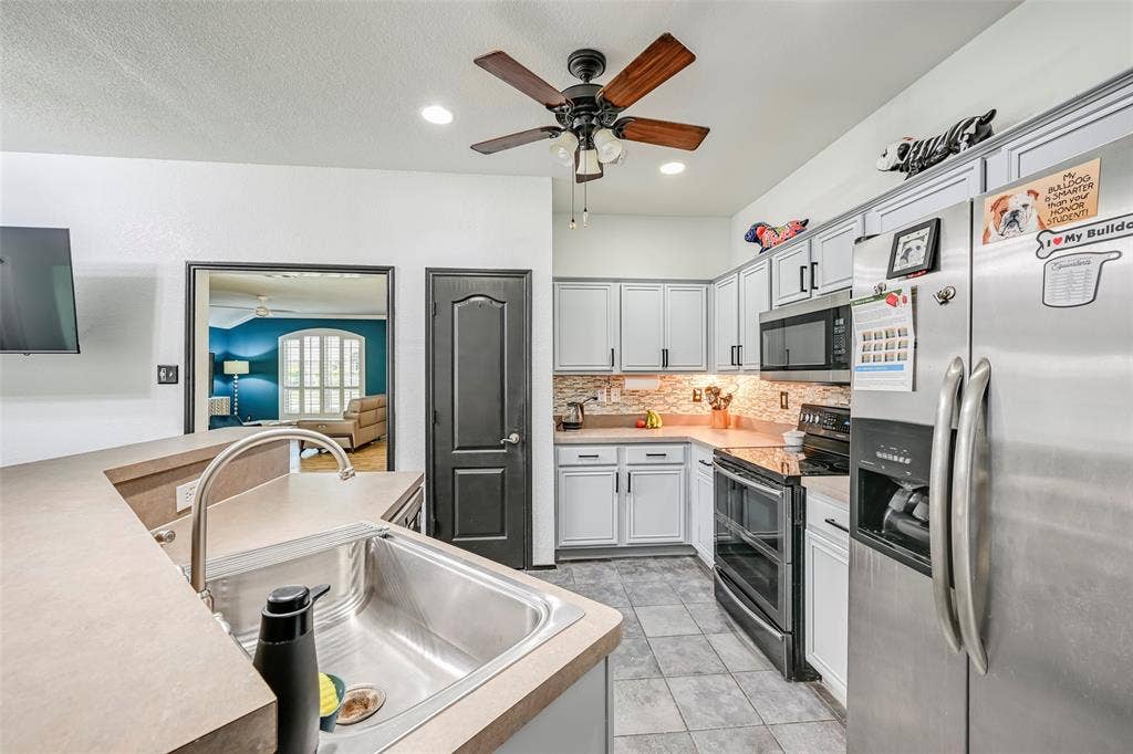 Well-appointed kitchen featuring light-colored cabinetry, stainless steel appliances, a tiled backsplash, and a ceiling fan