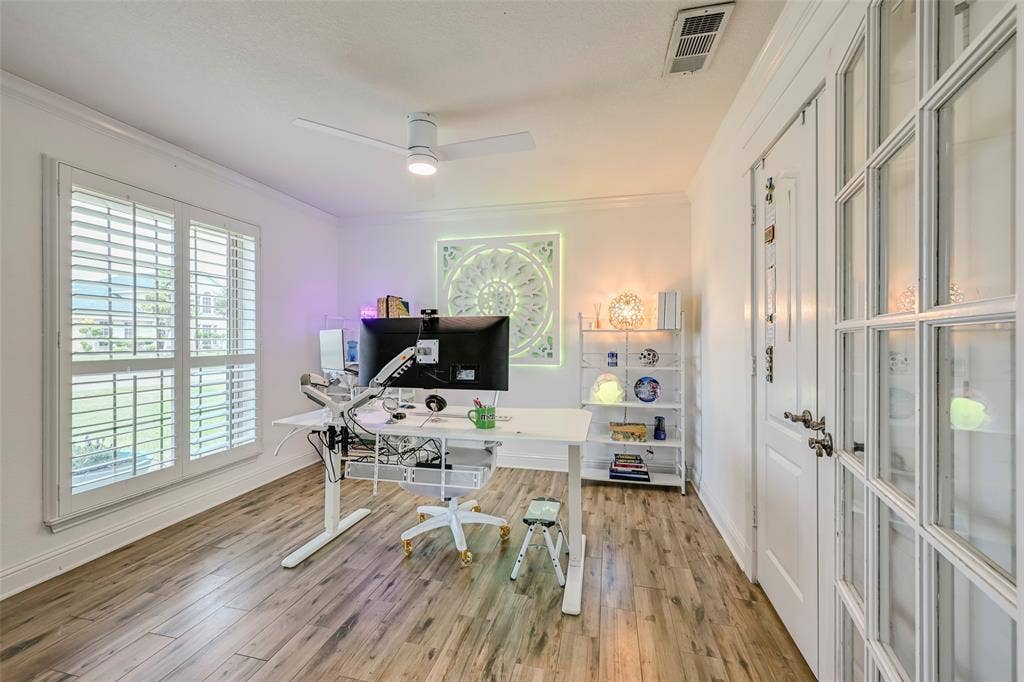 This room features wood-style flooring, a ceiling fan with integrated lighting, and a large window with white plantation shutters