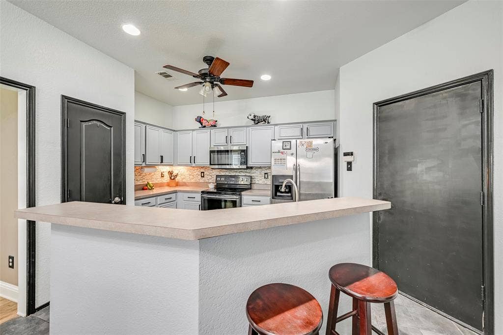 The kitchen features light-colored cabinetry, a tile backsplash, and stainless steel appliances
