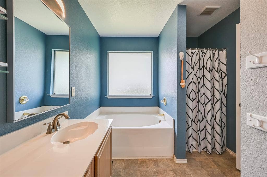 Bathroom featuring a vanity with a white countertop and an integrated sink, a bathtub, and a shower with a patterned curtain