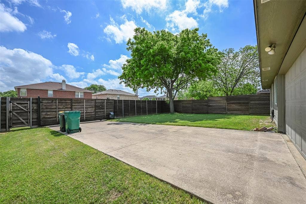 The property features a concrete patio area, a fenced yard with a lawn, and mature trees