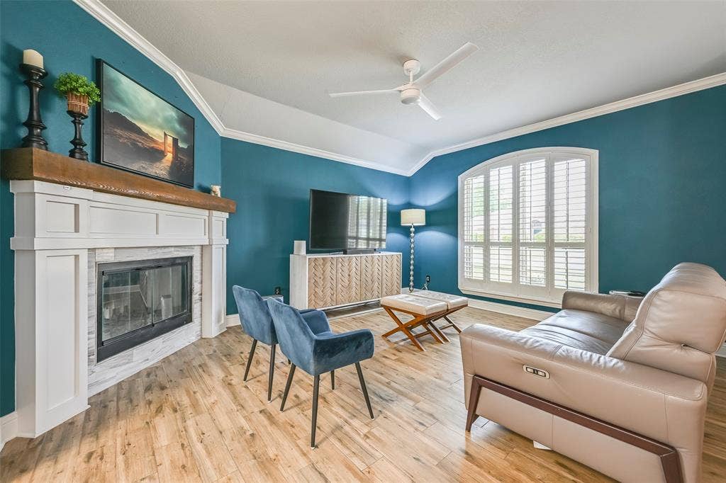 Living area featuring hardwood flooring, a white fireplace with a wood mantle, and a window with white shutters