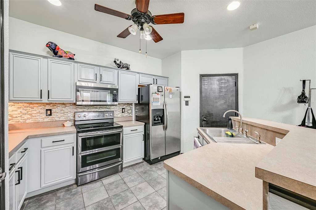 The kitchen features light-colored cabinetry with dark hardware, stainless steel appliances, and a tiled backsplash