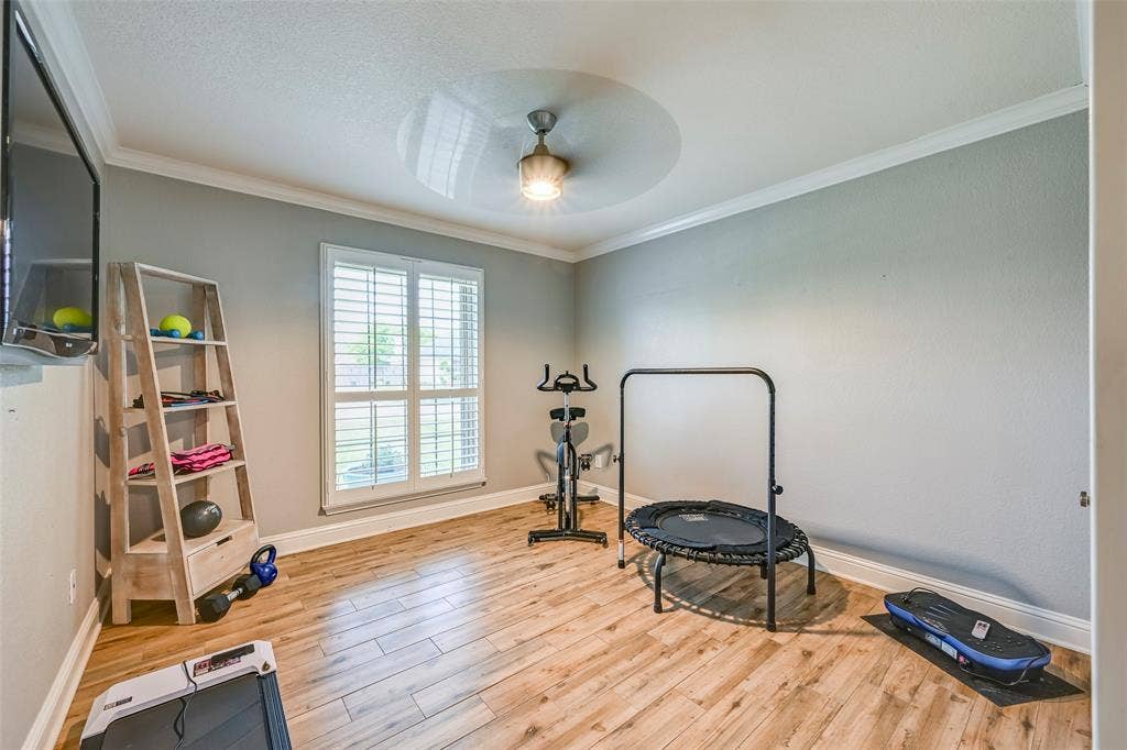 This room features wood-look flooring, crown molding, a window with plantation shutters, and a ceiling fan with integrated lighting