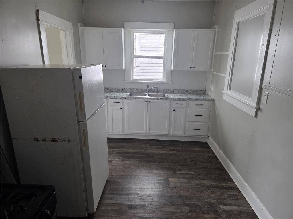 2523 Sanger Avenue, Waco, TX 76707 The kitchen features white cabinetry with dark hardware, a double basin sink, and wood-look flooring