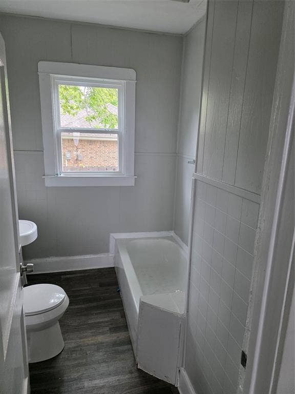 2523 Sanger Avenue, Waco, TX 76707 Bathroom featuring a window providing natural light, a bathtub, a toilet, a pedestal sink, and wood-look flooring