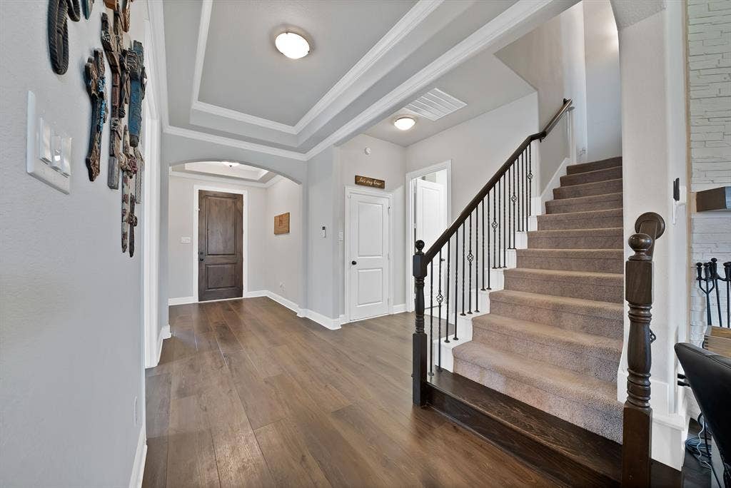 1905 Silver Falls Drive, Burleson, TX 76028 Entryway featuring hardwood floors, a tray ceiling, an arched doorway, and a carpeted staircase with a dark wood and wrought iron railing