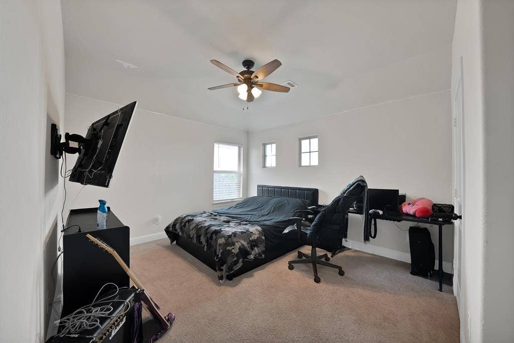 1905 Silver Falls Drive, Burleson, TX 76028 This room features light neutral-toned walls and carpeting, a ceiling fan with integrated lighting, and multiple windows allowing for natural light