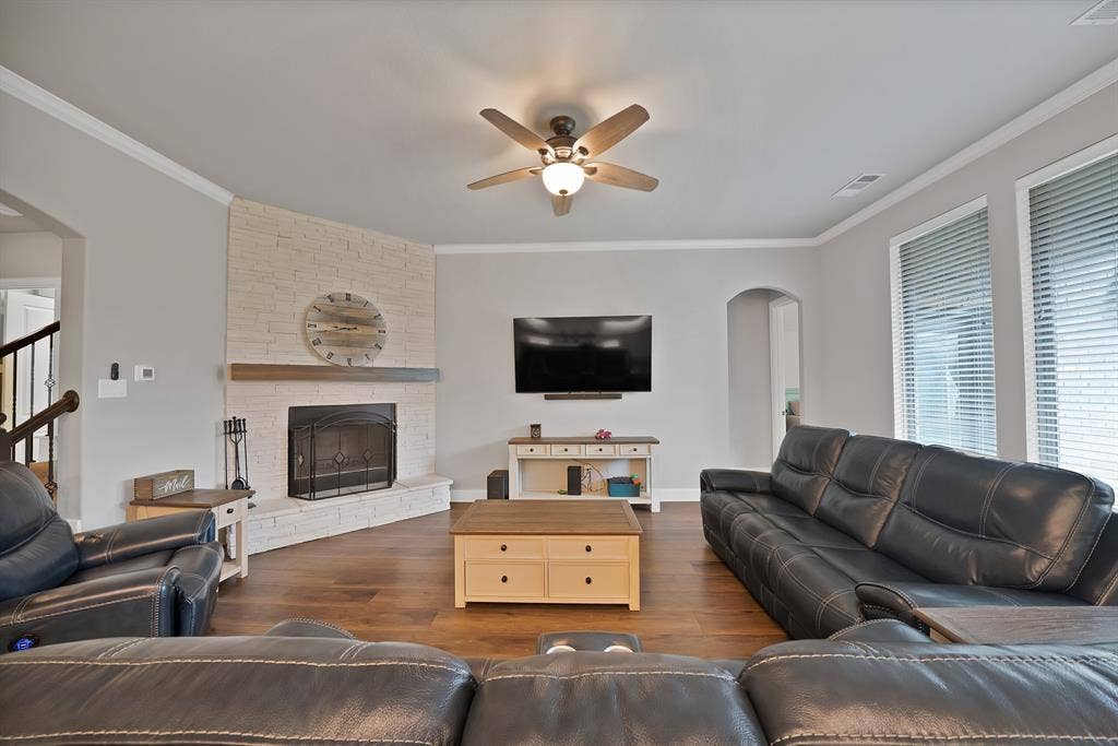 1905 Silver Falls Drive, Burleson, TX 76028 Living area featuring hardwood flooring, a corner fireplace with a white brick surround and wood mantel, crown molding, and a ceiling fan