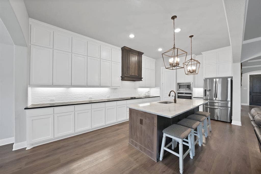 1905 Silver Falls Drive, Burleson, TX 76028 The kitchen features an expansive island with a light-colored countertop, white cabinetry, stainless steel appliances, and two decorative pendant lights