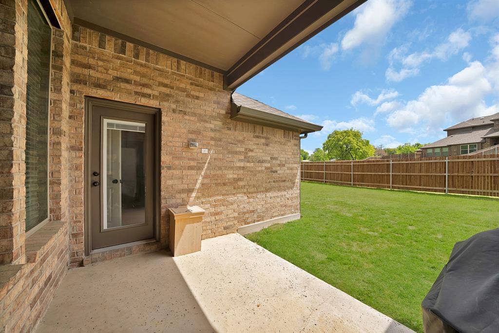 1905 Silver Falls Drive, Burleson, TX 76028 The property features a covered patio with a concrete surface, a brick exterior, and a glass-paneled door