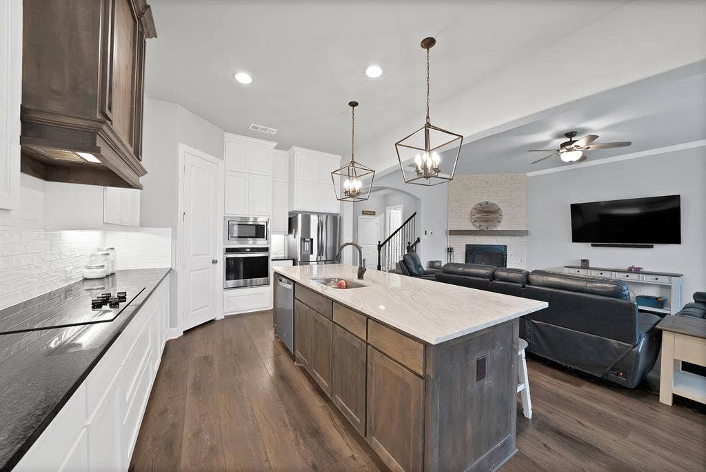 1905 Silver Falls Drive, Burleson, TX 76028 The kitchen features a large island with a light-colored countertop and pendant lighting, stainless steel appliances, and wood flooring