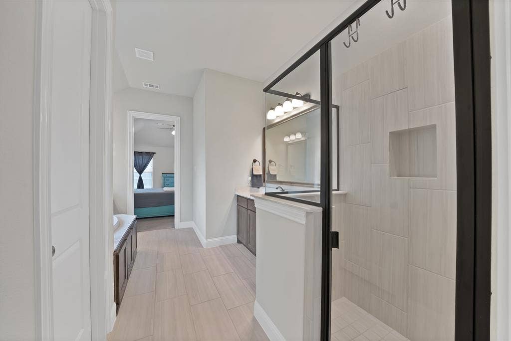 1905 Silver Falls Drive, Burleson, TX 76028 The bathroom features a spacious shower with a clear glass enclosure and light-colored tile work, a vanity with a mirror and lighting, and light wood-look flooring