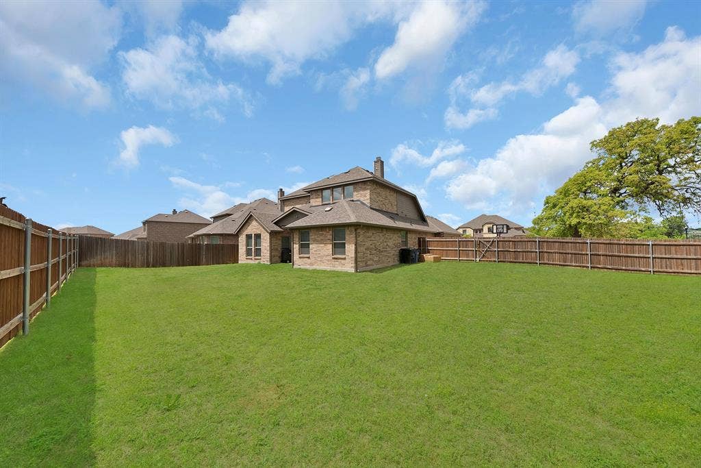 1905 Silver Falls Drive, Burleson, TX 76028 Expansive backyard with a lush green lawn, enclosed by a wooden fence, and featuring a two-story brick exterior with a pitched roof