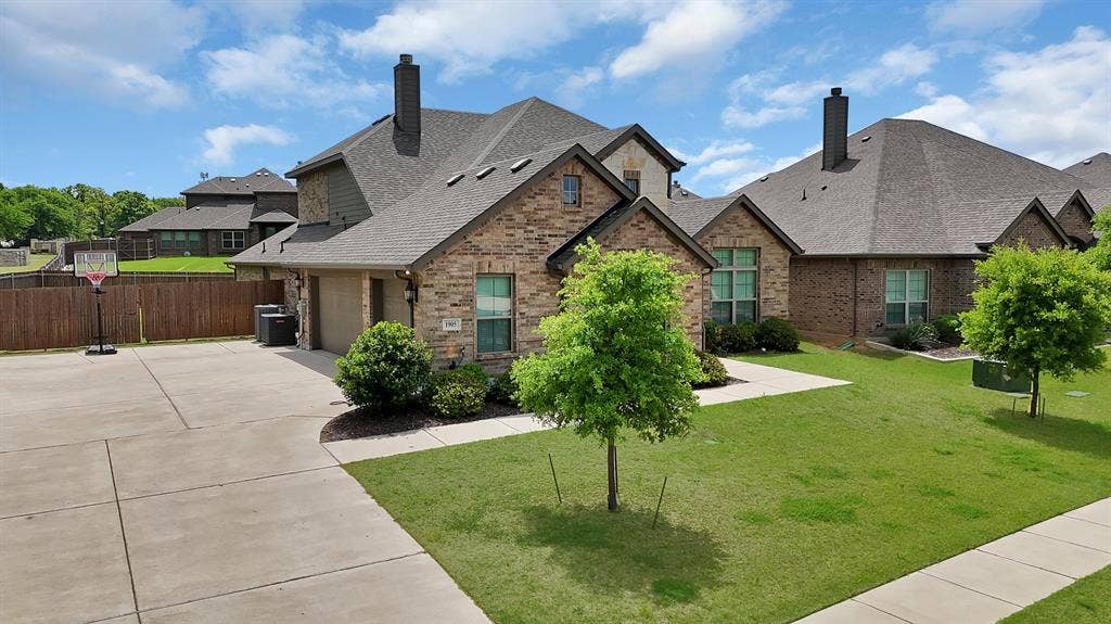 1905 Silver Falls Drive, Burleson, TX 76028 The property features a brick exterior, a driveway, and a front yard with a lawn and trees