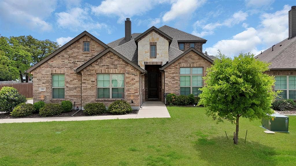 1905 Silver Falls Drive, Burleson, TX 76028 The property features a brick exterior with stone accents, a neatly manicured lawn, and mature landscaping with shrubs and a tree