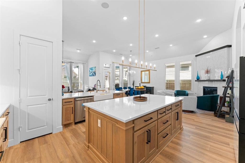 216 Shetland Lane, Northlake, TX 76247 Open concept living space featuring a kitchen island with a white countertop and wood cabinetry, hardwood floors, and a fireplace with a white tile surround