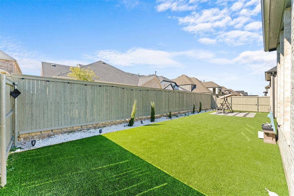 216 Shetland Lane, Northlake, TX 76247 The property features a spacious backyard with artificial turf, a light-colored privacy fence, and a decorative rock border with plantings