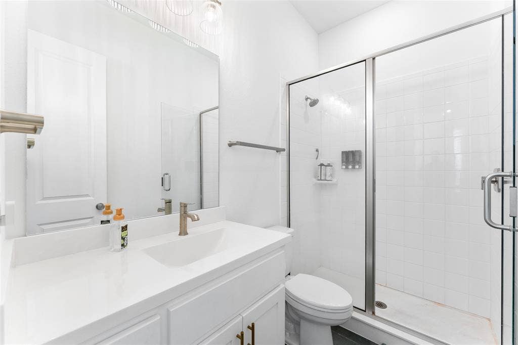 216 Shetland Lane, Northlake, TX 76247 Bathroom featuring a white vanity with a single basin sink, a large mirror, and a glass-enclosed shower with white tiled walls