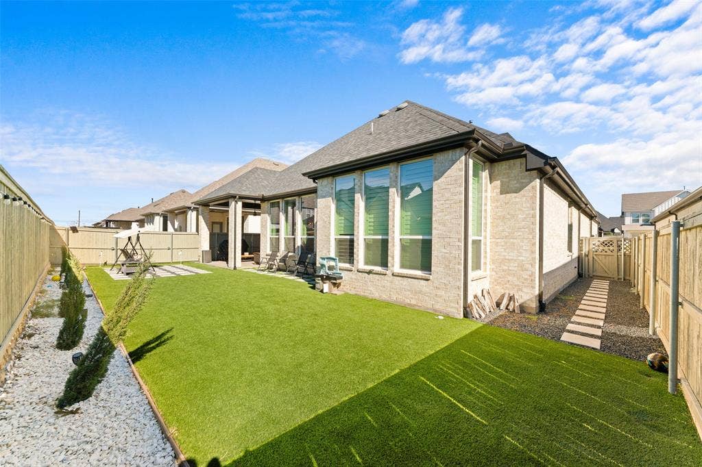 216 Shetland Lane, Northlake, TX 76247 The property features a spacious backyard with artificial turf, a rock border with planted shrubs, and a paved patio area