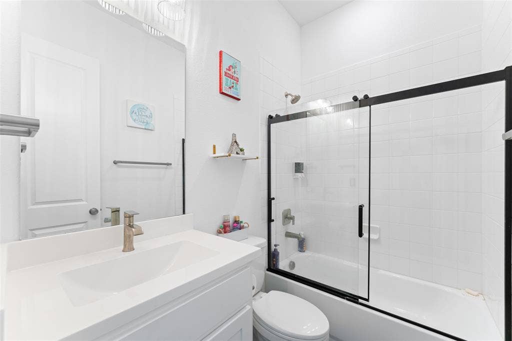216 Shetland Lane, Northlake, TX 76247 Bathroom featuring a vanity with a white countertop and an integrated sink, a large mirror, and a bathtub with a black-framed glass sliding door