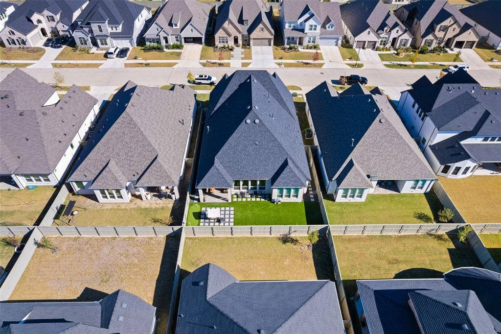 216 Shetland Lane, Northlake, TX 76247 Aerial view showcasing a residential property with a dark grey roof and a fenced backyard featuring a patio area and a lawn