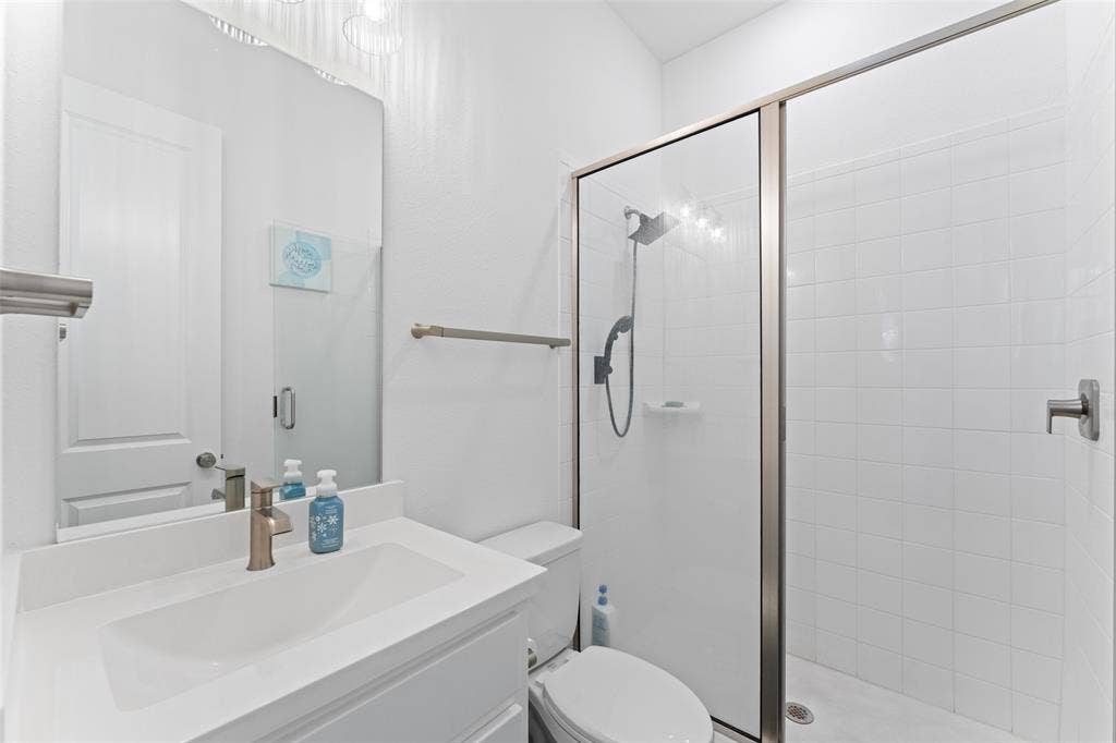 216 Shetland Lane, Northlake, TX 76247 Bathroom featuring a vanity with an integrated sink, a large mirror, a toilet, and a glass-enclosed shower with a tiled surround