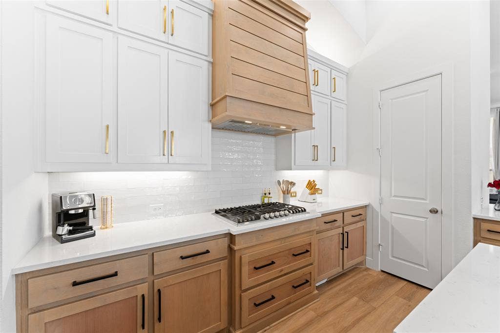216 Shetland Lane, Northlake, TX 76247 The kitchen features white upper cabinetry with gold-toned hardware, light wood-toned lower cabinetry with dark hardware, and white countertops