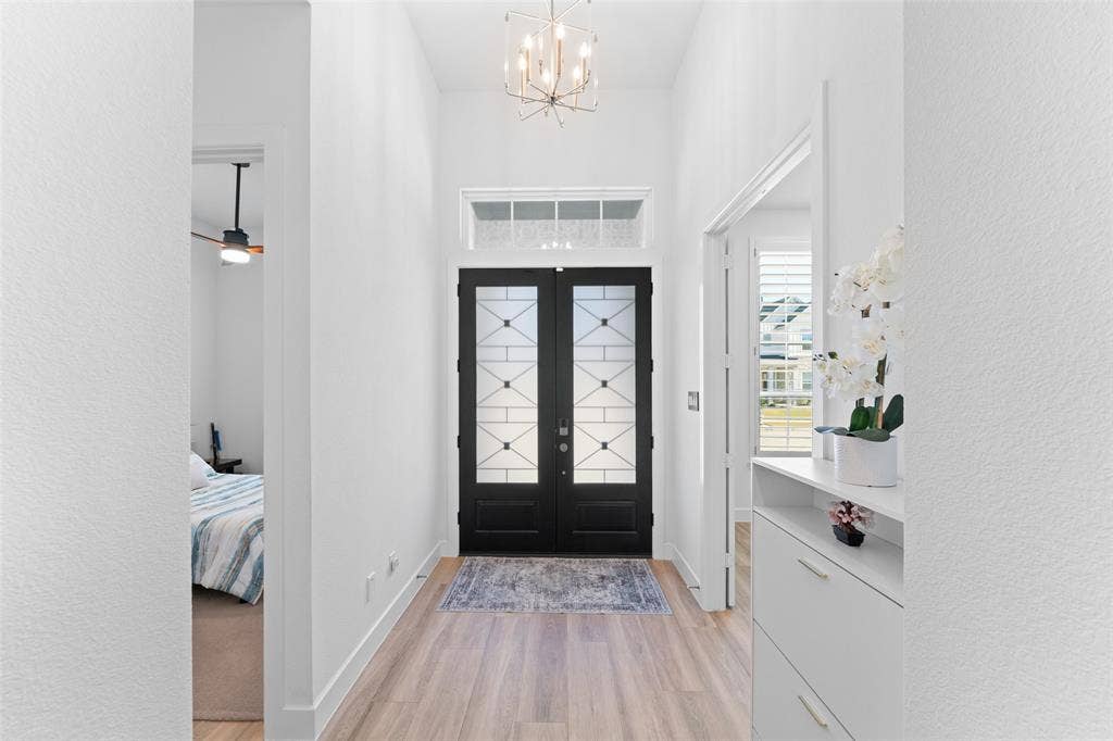 216 Shetland Lane, Northlake, TX 76247 The entryway features double black doors with decorative glass panels, light wood flooring, and a modern chandelier