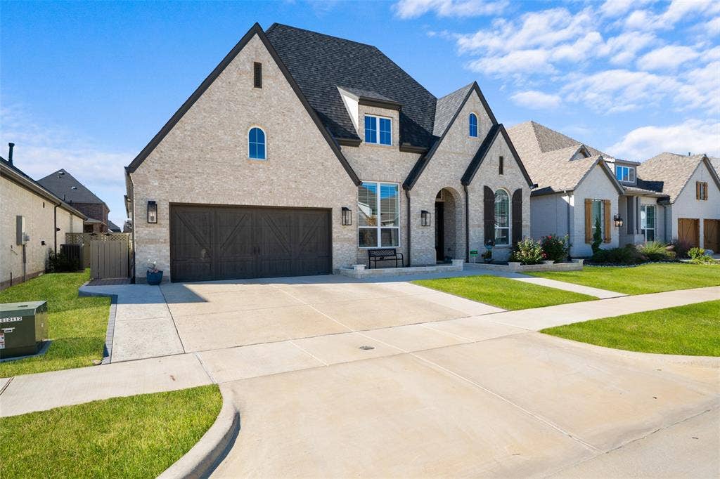 216 Shetland Lane, Northlake, TX 76247 This property features a light-colored brick exterior with dark trim and a dark roof, complemented by a concrete driveway and walkway