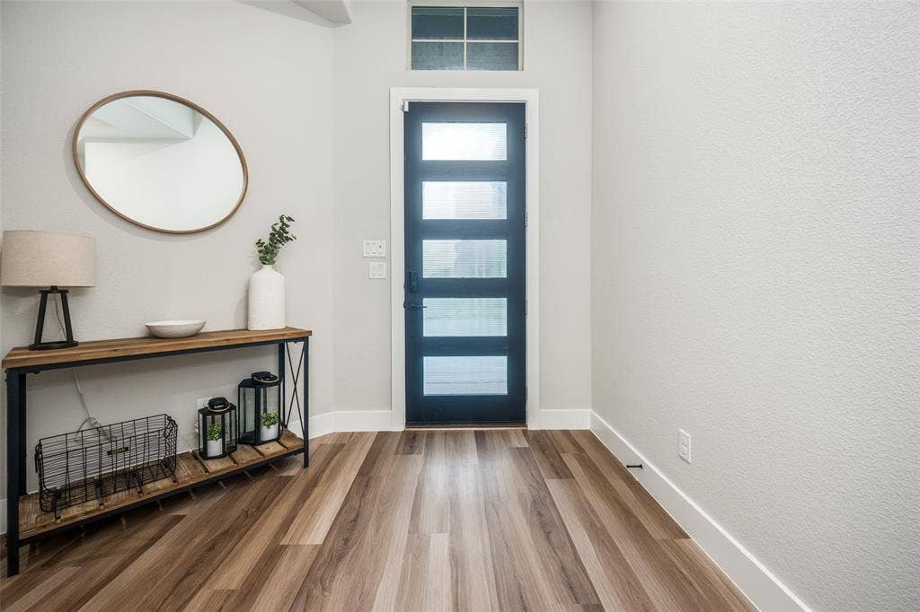 2801 Bedford Road, Northlake, TX 76226 Entryway featuring wood-finish flooring, a contemporary black door with frosted glass panels, an overhead transom window, and crisp white baseboards. Open, clean, and bright!