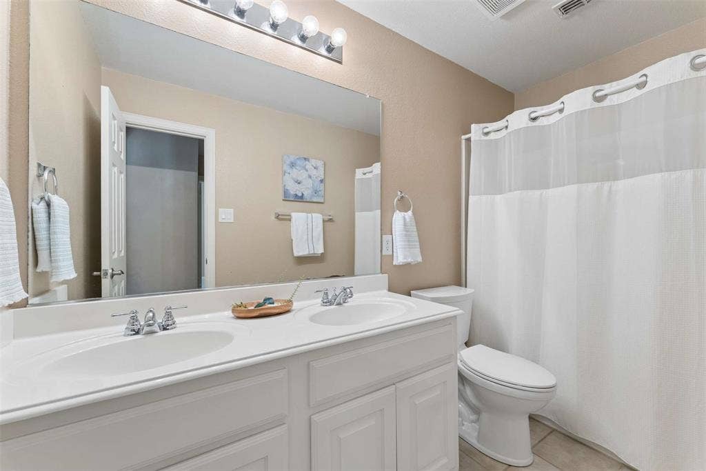 1221 Amistad Drive, Prosper, TX 75078 Bathroom featuring a vanity with dual sinks, a large mirror, and a shower with a shower curtain