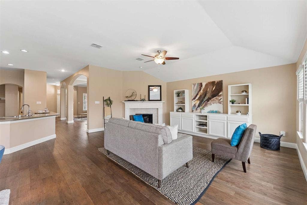 1221 Amistad Drive, Prosper, TX 75078 Spacious living area featuring hardwood flooring, a fireplace, and vaulted ceilings with a ceiling fan