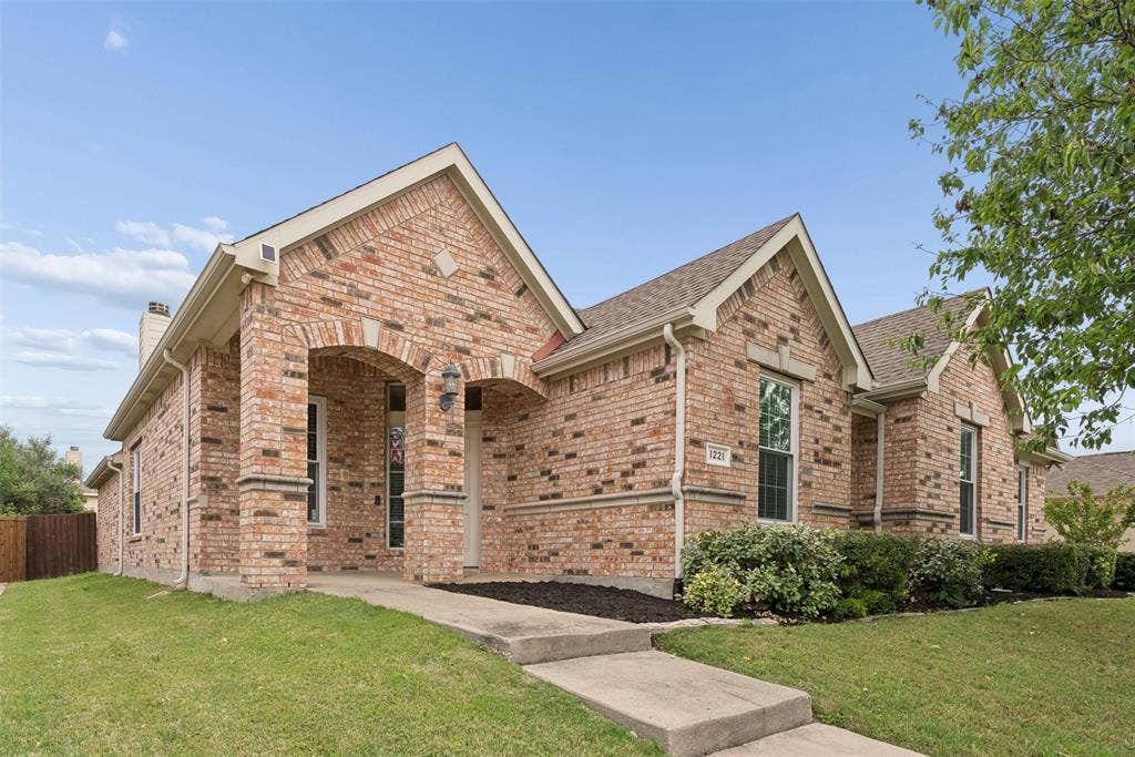1221 Amistad Drive, Prosper, TX 75078 The property features a brick exterior with architectural gables and an arched entryway